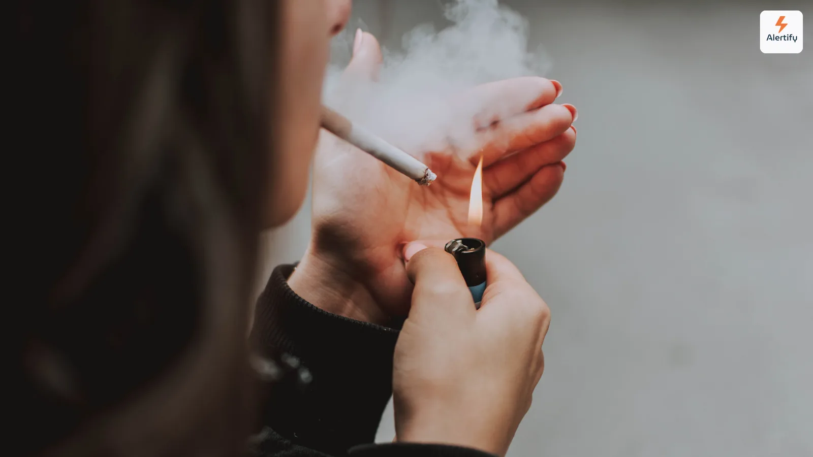 Persona encendiendo un cigarrillo en un interior con el humo enroscándose entre sus manos