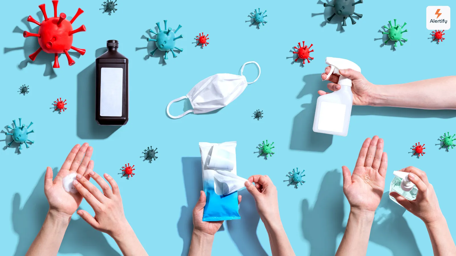 Vista cenital de modelos de virus, una mascarilla, un espray desinfectante y manos usando productos de higiene