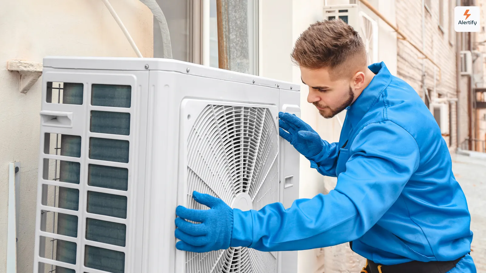 Técnico de climatización con mono azul y guantes revisando una unidad exterior de aire acondicionado