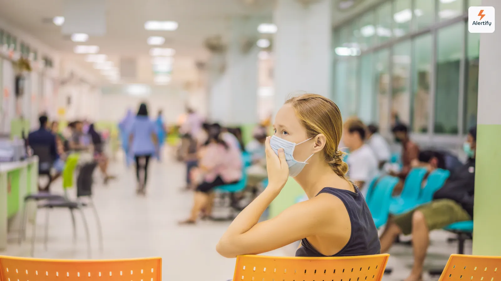 Mujer con mascarilla sentada en una concurrida sala de espera de hospital