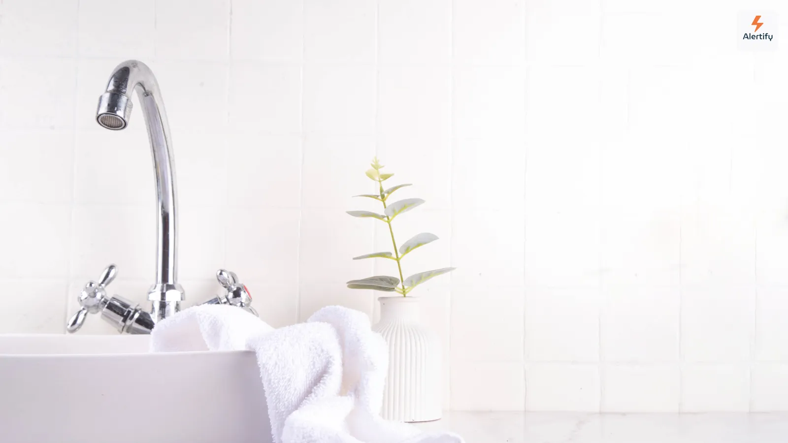 Un baño luminoso con azulejos blancos, un lavabo, una toalla doblada y una planta en maceta pequeña: el tipo de estancia húmeda donde el moho aparece primero.