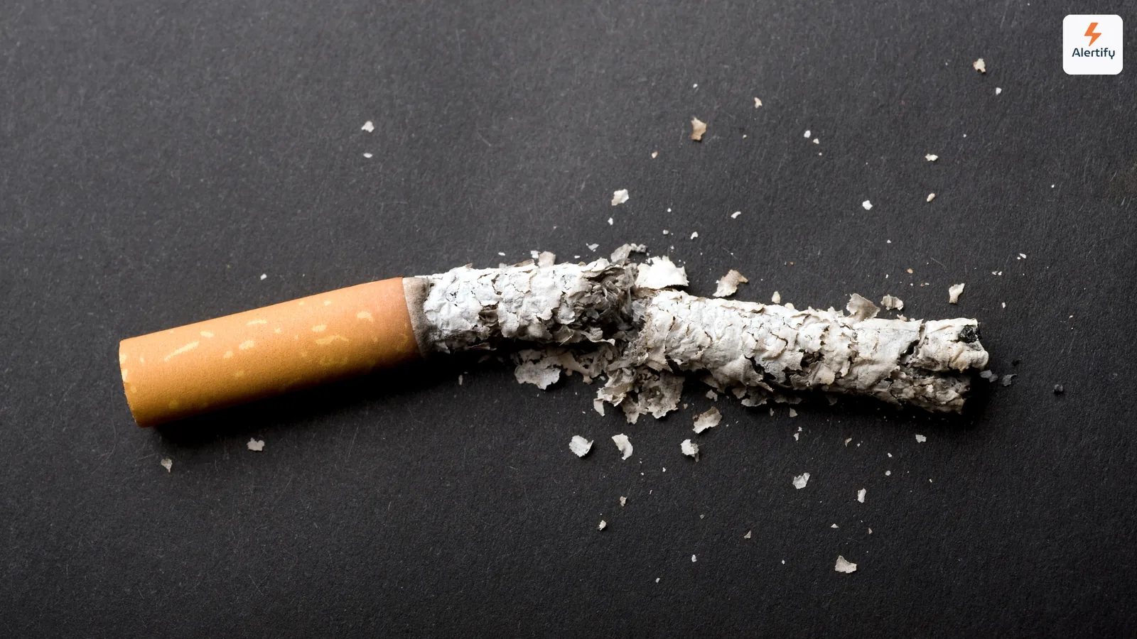 Cigarrillo roto por la mitad con ceniza esparcida sobre una superficie oscura